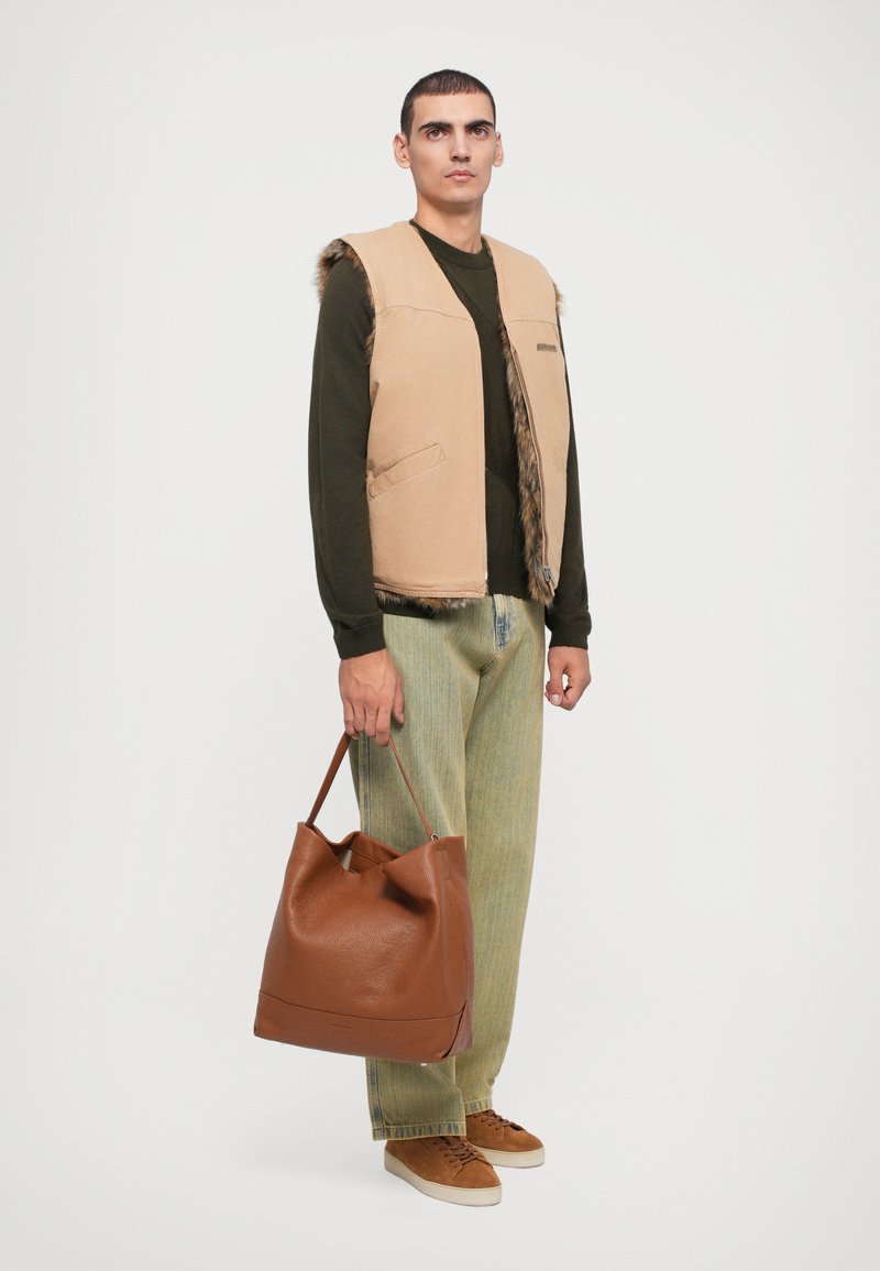 Beige vest with faux fur trim, green long-sleeve shirt, light green pants, and brown leather tote bag, featuring a soft, textured surface.