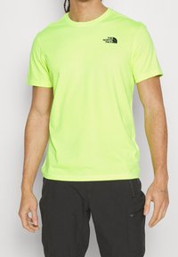 Neongelbes T-Shirt mit kurzen Ärmeln aus weichem Stoff, mit kleinem schwarzem Logo auf der linken Brust. Klassisches Rundhals-Design.