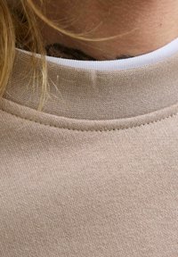 Heledbeez töötlusega kangast heledat beeži pulloverit, millel on soonikkoes ümmargune kaelus, millel on valge sisekaelus.