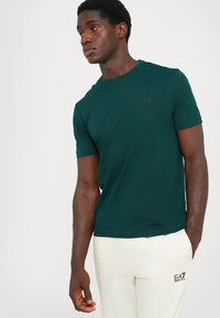 Dark green short-sleeve T-shirt made of soft fabric. It features a subtle black logo on the chest and a relaxed fit.