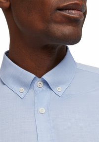 Himmelblaues, strukturiertes Hemd mit button-down Kragen, weißen Knöpfen und einer gut sitzenden Passform. Nahaufnahme, die die Stoffdetails betont.