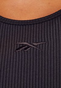 Tessuto a costine nero, con scollo rotondo e un dettaglio del logo ricamato. La trama è sottile con linee verticali.