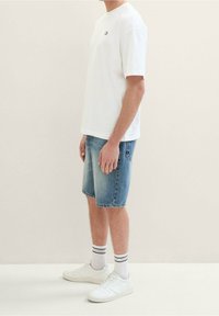 Valkoinen puuvillapaita lyhyillä hihoilla, siniset farkkushortsit, valkoiset lenkkarit ja ribbikuvioiset valkoiset sukat, joissa on mustat raidat.