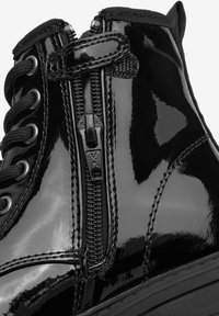 Bottine en cuir verni noir avec fermeture éclair et lacets, dotée d'une finition lisse et brillante ainsi que d'une semelle en caoutchouc robuste.