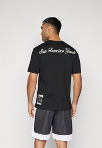 Svart kortermet t-skjorte med "San Francisco Giants" i hvit skrift på baksiden. Kombinert med grå mesh-shorts med hvite detaljer.