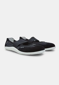 Zapatos ligeros negros con parte superior de malla transpirable, puntera redondeada y suela de goma blanca en contraste. Presentan una correa elástica a lo largo del pie.