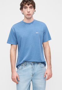 Μπλε βαμβακερό μπλουζάκι με κοντά μανίκια και στρογγυλή λαιμόκοψη, με μικρό λευκό λογότυπο "obey" στο αριστερό μέρος του στήθους. Συνδυάζεται με ανοιχτόχρωμο μπλε τζιν.