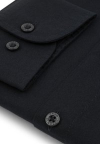 Czarny materiał o gładkiej fakturze z klapką i dwoma okrągłymi czarnymi guzikami z wytłoczonym napisem "PAKO". Prosty, minimalistyczny design.