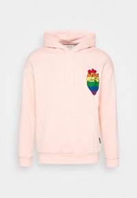 Sudadera rosa claro con un bolsillo frontal y capucha con cordón. Presenta un bordado de corazón arcoíris multicolor en el lado izquierdo.