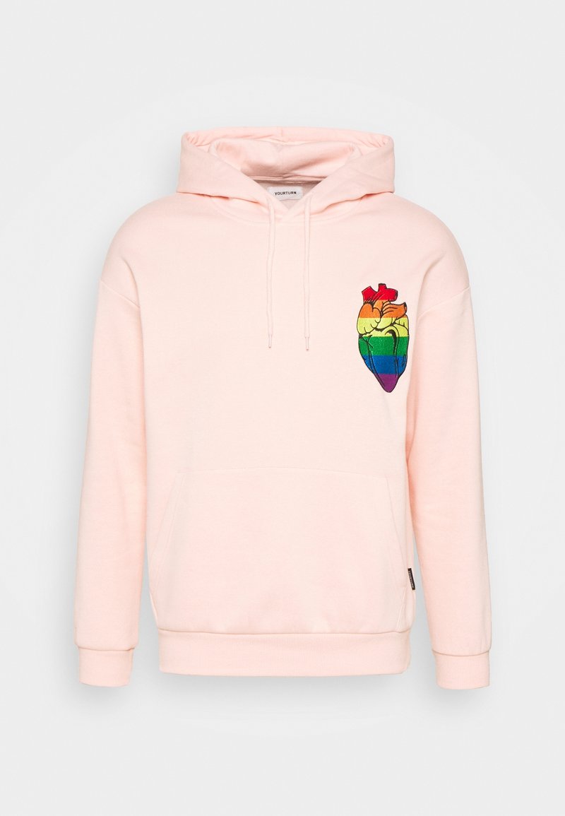 Sudadera rosa claro con un bolsillo frontal y capucha con cordón. Presenta un bordado de corazón arcoíris multicolor en el lado izquierdo.