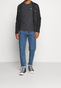 Svart denimjacka över en mörkgrå t-shirt, ljusblå jeans med uppvikta ärmar och svarta hög-top sneakers med vita sulor.