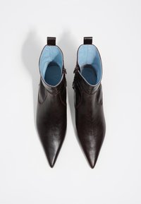 Botas de cuero marrón hasta el tobillo con punteras afiladas y forro de tela azul. Cuentan con un cierre lateral y acentos texturizados a lo largo del tobillo.