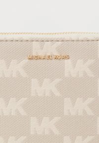 Portefeuille zippé beige avec un motif de logo "MK", tissu texturé et marque en ton doré. Les accents incluent une fermeture éclair dorée.