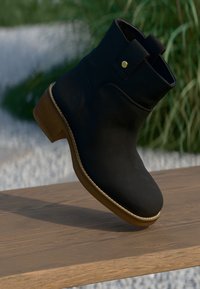 Bottine noire à bout arrondi, fabriquée en cuir lisse, avec une semelle cousue et un petit bouton doré en accent sur le côté.