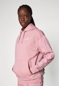 Rosa bomull hettegenser med kengurulomme, snorhette og logo på brystet og ermet. Glatt tekstur med ribbede mansjetter.