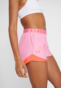 Rosa träningsshorts med orange kant och midjeband. Har en broderad logotyp på sidan. Tillverkade av lätt och ventilerande material.