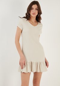 Lichte beige jurk met V-hals en korte mouwen, gemaakt van een gestructureerde stof en met een volantszoom, ontworpen voor een losse pasvorm.