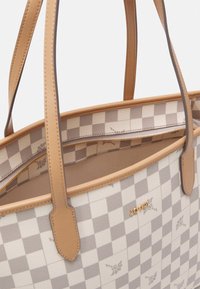 Totesäck med ett beige och grått rutmönster med blommiga detaljer, handtag i tanläder och ett innerfack med dragkedja.