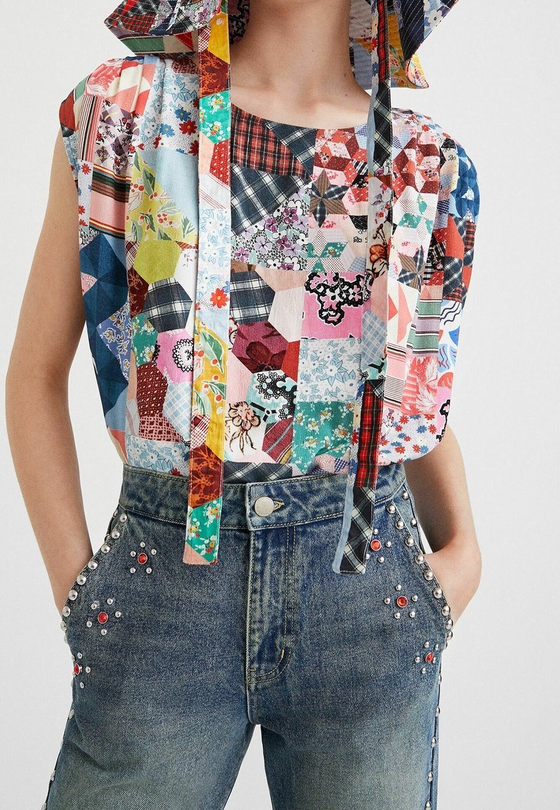 Blusa senza maniche in patchwork con motivi floreali, a quadri e geometrici, abbinata a jeans a vita alta con embellishments in argento e rosso a borchie.