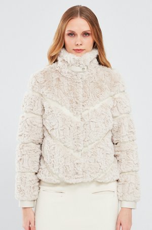 Faux fur jas in lichtbeige met een hoge kraag, voorzien van chevronpatronen en een zachte textuur. Ontworpen met drukknoopsluitingen en omgeslagen mouwen.