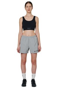 Vrouw staand in een zwarte sportbeha, lichtgrijze shorts met elastische taille, witte sokken en zwarte sneakers tegen een witte achtergrond.