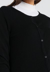 Cardigan nero con scollo rotondo, chiusura con bottoni e maniche lunghe; realizzato in materiale morbido, con una texture a coste.