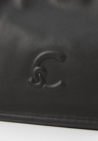 Borsa a spalla nera in pelle con una superficie liscia, caratterizzata da un logo in rilievo di forma stilizzata a lettera 'C'.