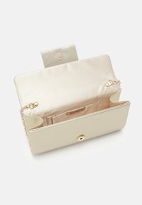 Pochette beige ouverte avec sangle chaîne dorée et fermeture pression, montrant une doublure intérieure lisse et une petite poche intérieure étiquetée Menbur.