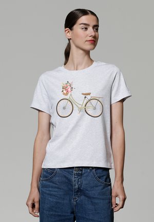 T-shirt gris clair à manches courtes avec un motif de bicyclette portant un panier de fleurs. Tissu doux et coupe décontractée, associé à un jean bleu.