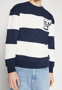 Felpa a righe blu navy e bianche in cotone. Presenta polsini e orlo a coste, con un logo ricamato sul petto. Design classico con collo a giro.