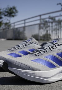 Gray athletic shoes with blue accents and three stripes design. Lightweight mesh upper, textured surface, and black rubber sole.