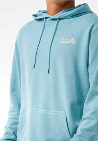 Jasnoniebieska bluza z kapturem z kieszenią z przodu, sznurkami i małym logo "Rip Curl" w pastelowych kolorach na piersi. Miękka tekstura materiału.