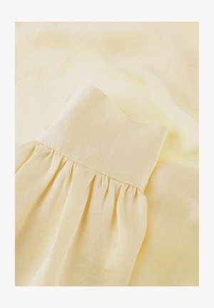 Tissu jaune pâle doux avec un détail froncé, créant de plis délicats et une texture sur un fond lisse.