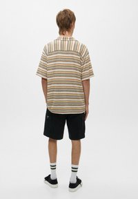 Korte mouwen shirt met horizontale strepen in bruin, geel en blauw; gecombineerd met zwarte cargoshorts en gestreepte sokken. Minimalistisch ontwerp.