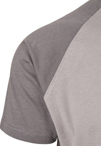 T-shirt z krótkim rękawem z szarym panelem na ramieniu i jaśniejszą częścią tułowia, wykonany z miękkiego materiału o gładkiej fakturze i kontrastowych przeszyciach.