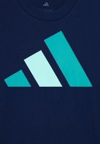Tamsiai mėlyna medvilninė marškinėliai su dideliu žalsvai mėlynu geometriniu logotipo dizainu, kuriame pavaizduotos trys persidengiančios figūros skirtingais dydžiais.