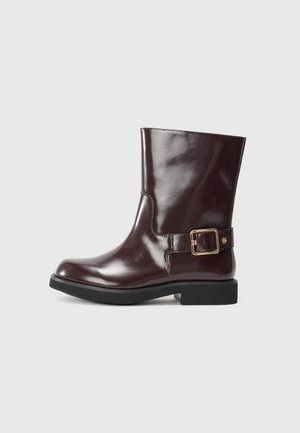 Bottines en cuir bordeaux avec une finition brillante, présentant un détail de boucle sur le côté et un petit talon noir solide. Texture lisse.