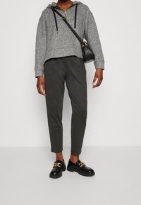 Gråspettrad huva med dragkedja, kombinerad med mörkgrå avsmalnande byxor och svarta loafers med en guldkedjeaccent.