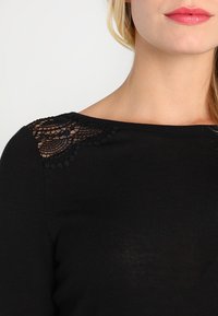 Czarny sweter dzianinowy z koronkowym detalem na jednym ramieniu. Gładka tekstura, szeroki dekolt i dopasowany krój.