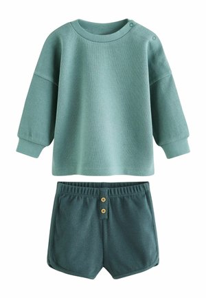 Dopasowany top o długim rękawie w kolorze zielonkawoniebieskim z fakturą i napami na ramieniu, zestawiony z ciemnozielonkawoniebieskimi, fakturowanymi szortami z elastycznym pasem i dwoma guzikami z przodu.