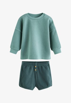 Haut texturé à manches longues de couleur bleu sarcelle avec des boutons-pression à l'épaule, associé à un short texturé bleu sarcelle foncé avec une taille élastique et deux boutons à l'avant.