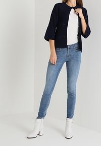 Marinblå ribbad cardigan med klockärm, kombinerad med ljusblå skinny jeans. Bärs med vita ankelstövlar med blockklack.