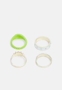 Conjunto de quatro anéis: um verde texturizado em borracha, um dourado metálico com espigões, um branco brilhante com strass e um anel metálico liso.