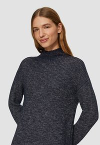 Maglione lavorato a maglia di colore navy con collo alto, maniche ampie, motivo testurizzato e vestibilità rilassata. Materiale morbido con striature di colore più chiaro sparse. 