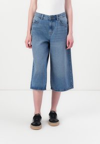 Blå denim culotter med høy midje, med knappeåpning, lommer og r�å kanter. Brukt med svarte sneakers for kontrast.
