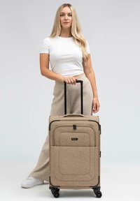 Beige stoffen koffer met een gestructureerde afwerking, zwarte hardware, ritscompartimenten en soepel rollende wielen. Inclusief uitschuifbare handgreep.