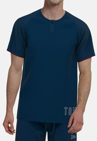 Camiseta de manga corta azul marino con escote redondo, tapeta de dos botones y detalles en burdeos contrastantes en las mangas. Detalle de texto blanco en el lado.
