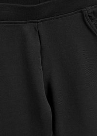 Schwarze Baumwoll-Sweatpants mit einer glatten Textur, elastischem Bund und Seitentaschen. Nahtdetails sind entlang der Stoffoberfläche sichtbar.