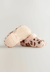Sabots roses avec un motif léopard, présentés de côté avec des semelles texturées visibles, sur un fond clair.