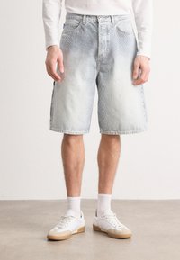 Shorts din denim de culoare albastru deschis, cu spălare uzată, croială dreaptă, buzunare frontale și talie, asortați cu adidași albaștri și șosete tip crew.